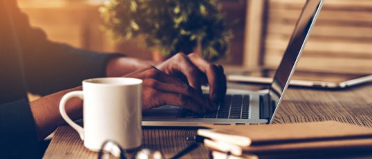 Close-up side view part of young African man using laptop while sitting at his working place